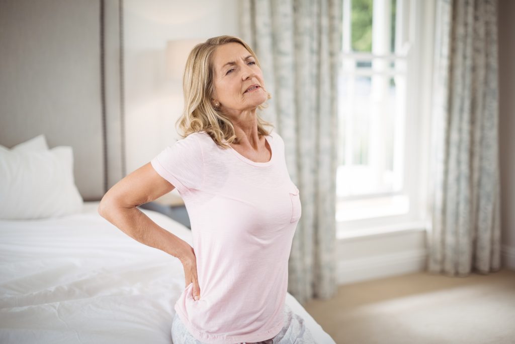 Senior woman having back pain in bedroom at home